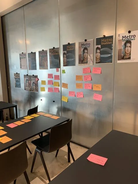 Seminarraum: An einer Metallwand hängen Plakatentwürfe «Metro Shadows» in mehreren Varianten, darunter farbige Post-its mit Notizen; auf den Tischen davor weitere Post-its.