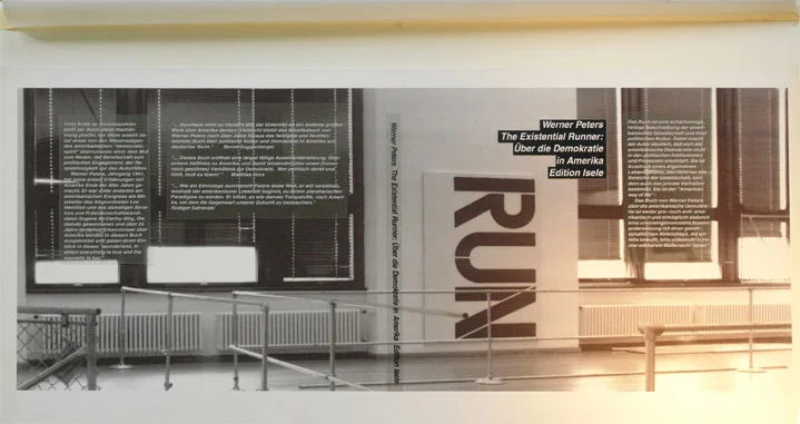 Schwarzweißfoto einer Ausstellungssituation: hohe Stoffbahnen mit dem gedrehten Schriftzug «RUN» vor einer Fensterfront, daneben schmale Textspalten.